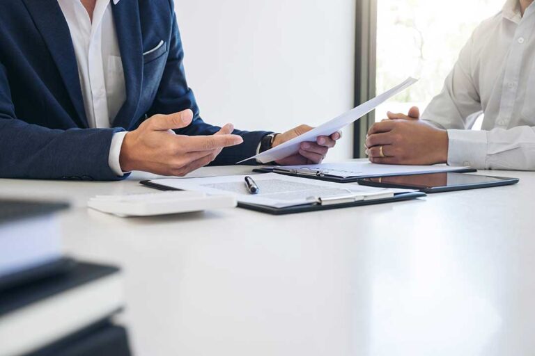 A person reviews a printed insurance document at a home desk with a calendar and overdue bill.